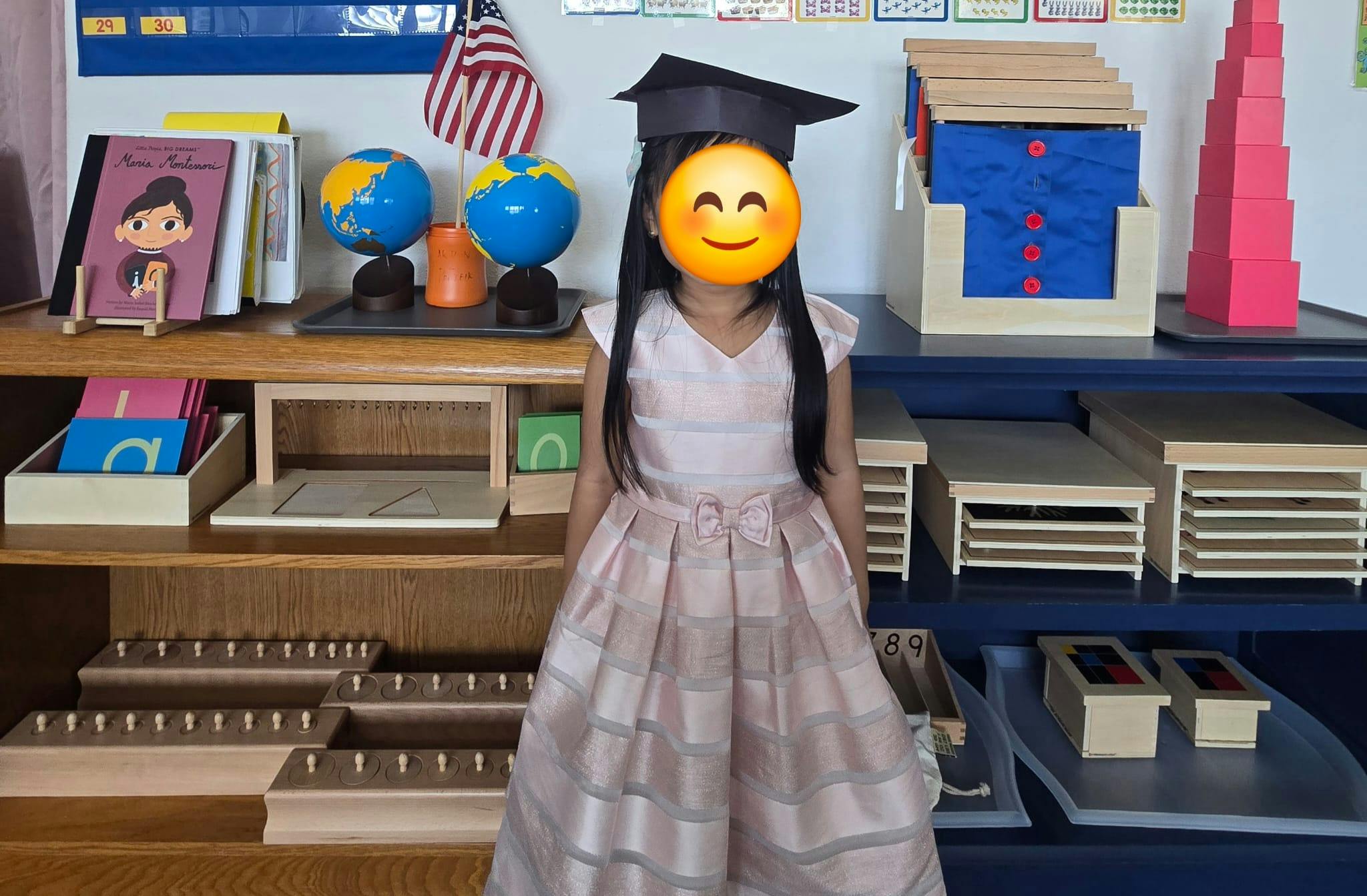 Child in a graduation cap and dress standing in a classroom
