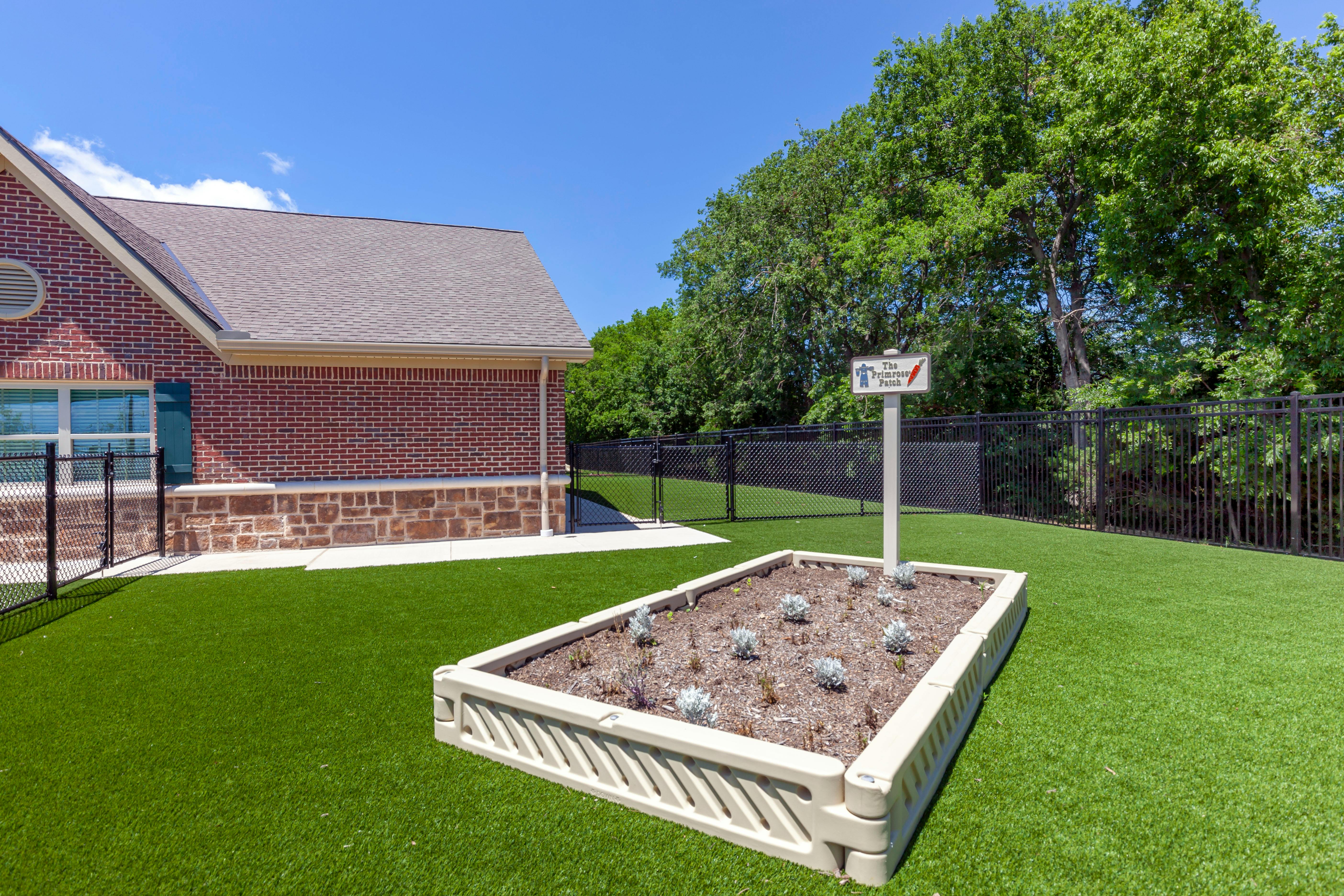 Raised garden bed with small plants and a sign that says "The Primrose Patch"