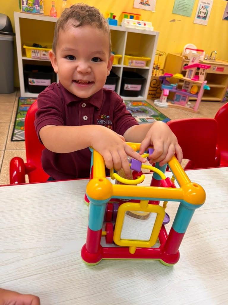 Child playing with a colorful bead maze toy at a table in a classroom