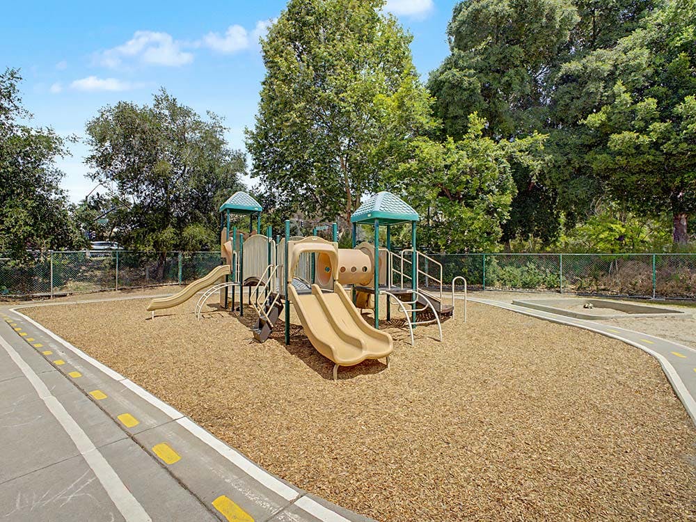 A tan and green outdoor playground with slides and wood chips