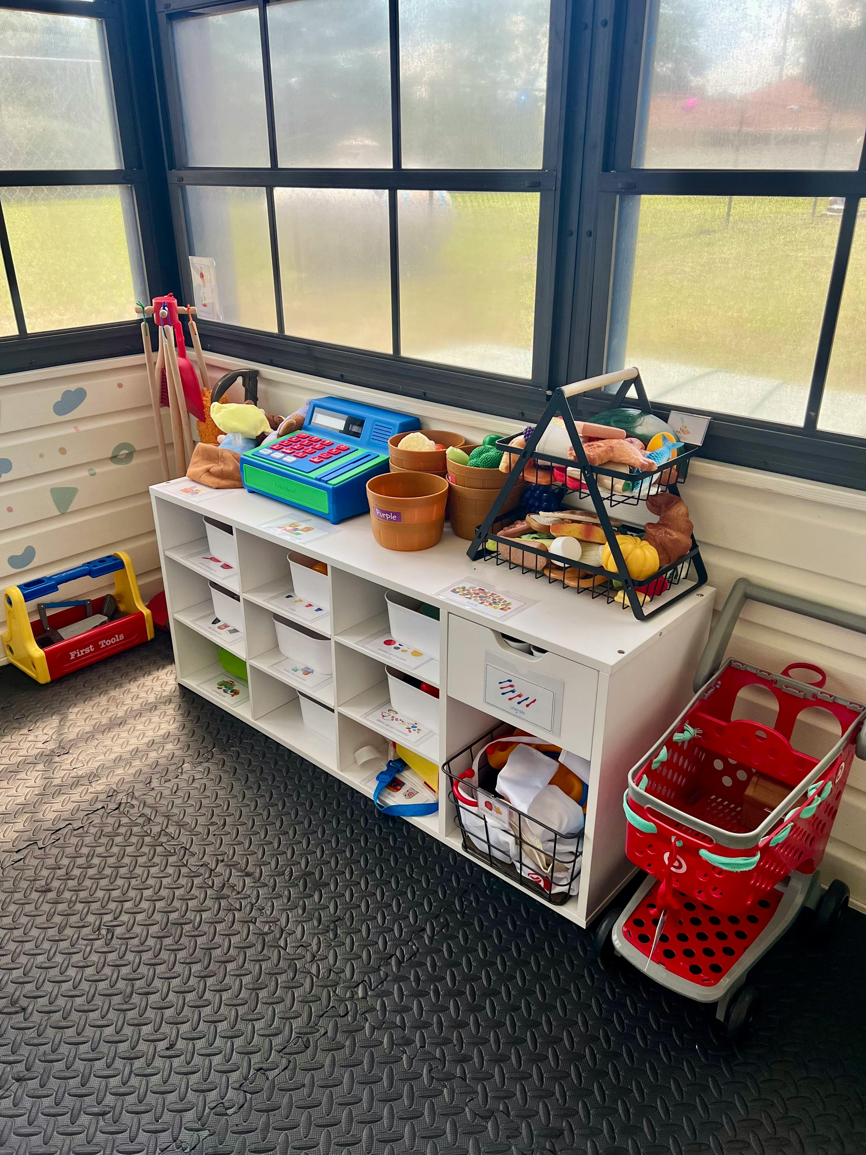 Play kitchen with toy cash register, shopping cart, and food items on a shelf