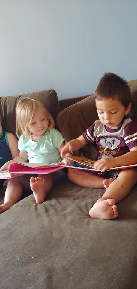 Two children sitting on a couch reading books