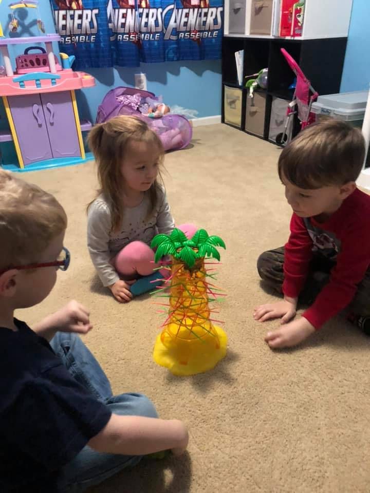 Three children sitting on the floor playing a game with a pineapple-shaped toy