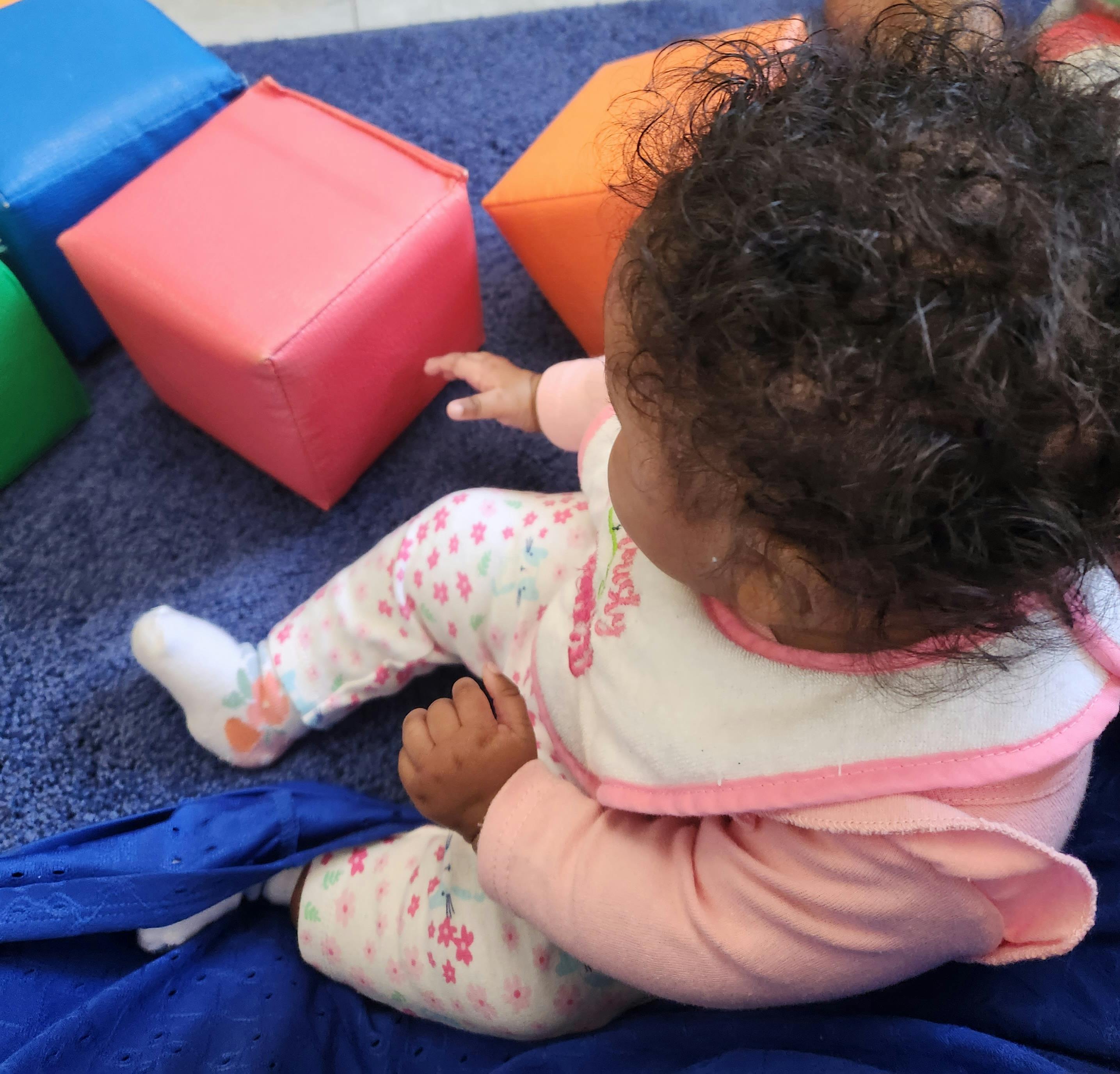 Child on a blue mat reaching for a red block