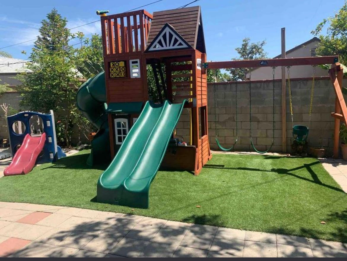 Wooden playground set with green slides and swings on artificial turf