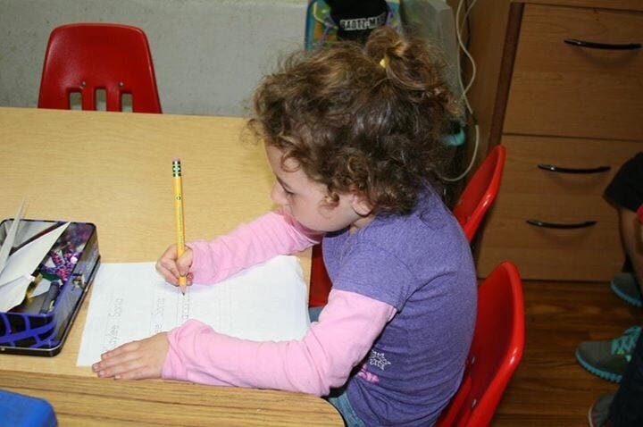 Child writing on paper with a pencil at a desk