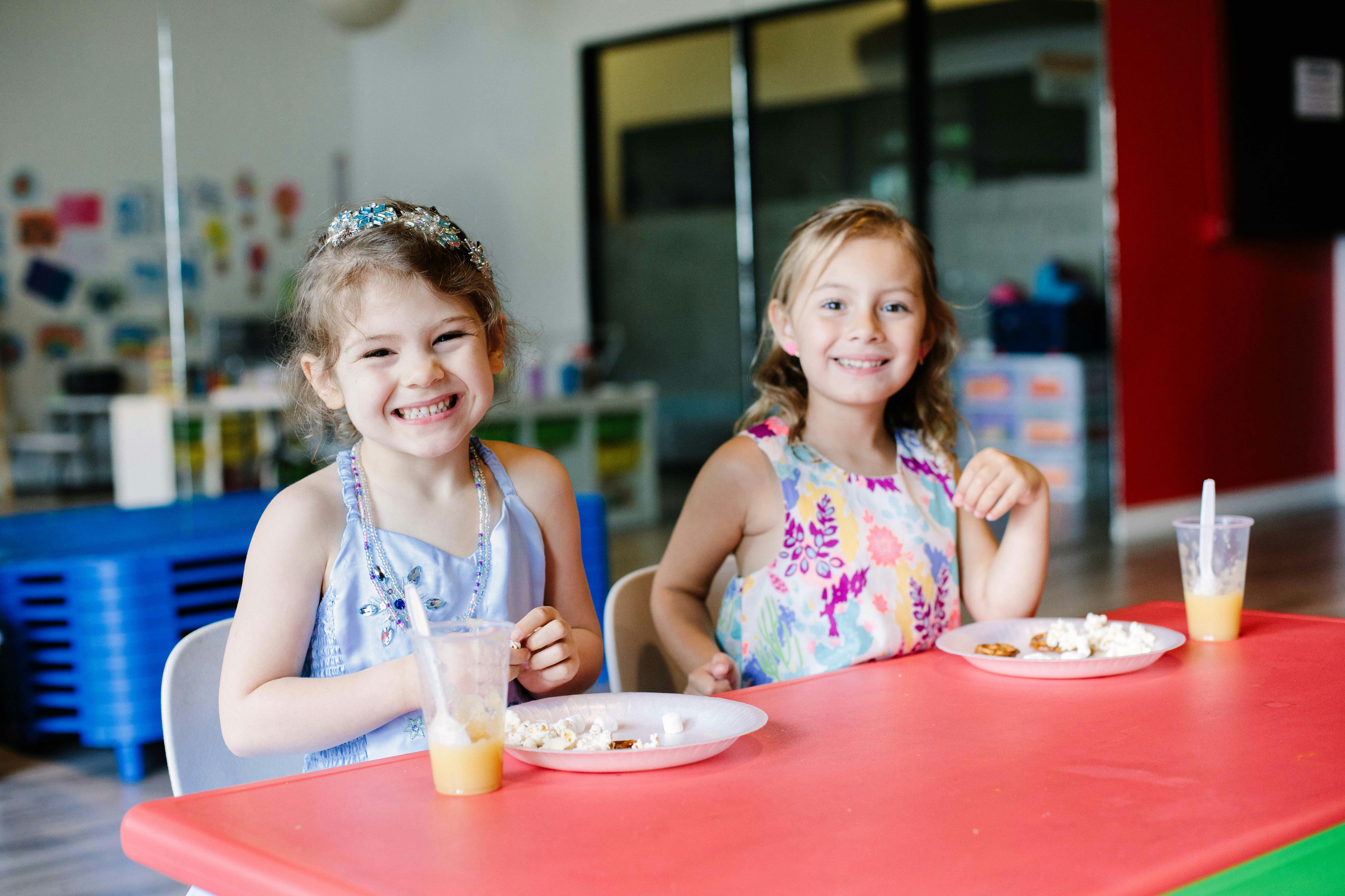 Two children sitting at a red table with plates and drinks