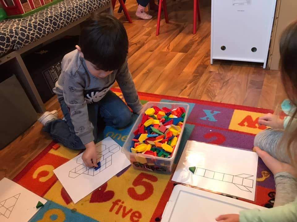 Child kneeling on a rug, placing a small object on a paper with a pattern