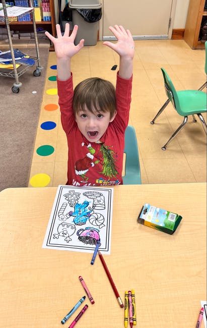 Child with arms raised above a coloring page and crayons on a table