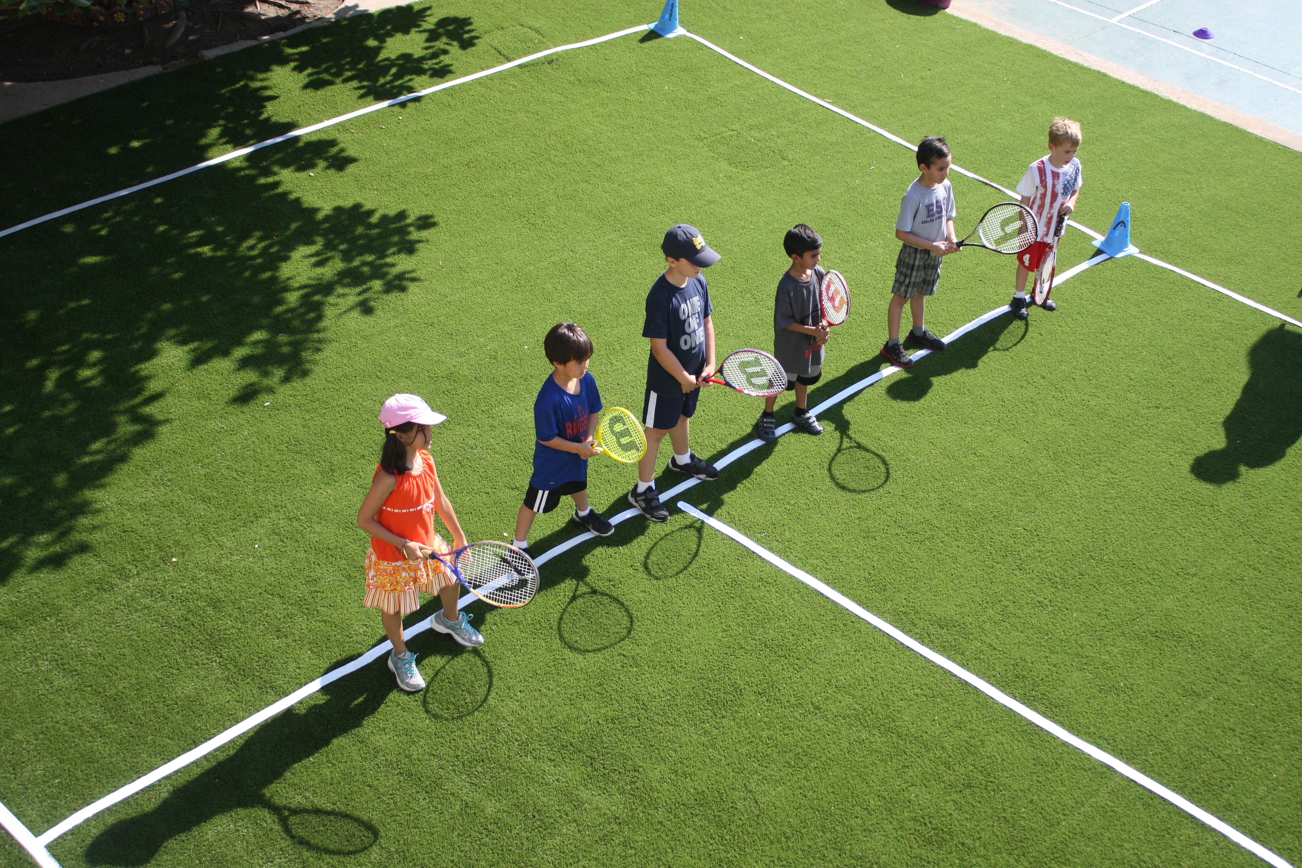 Children holding tennis rackets on a green court