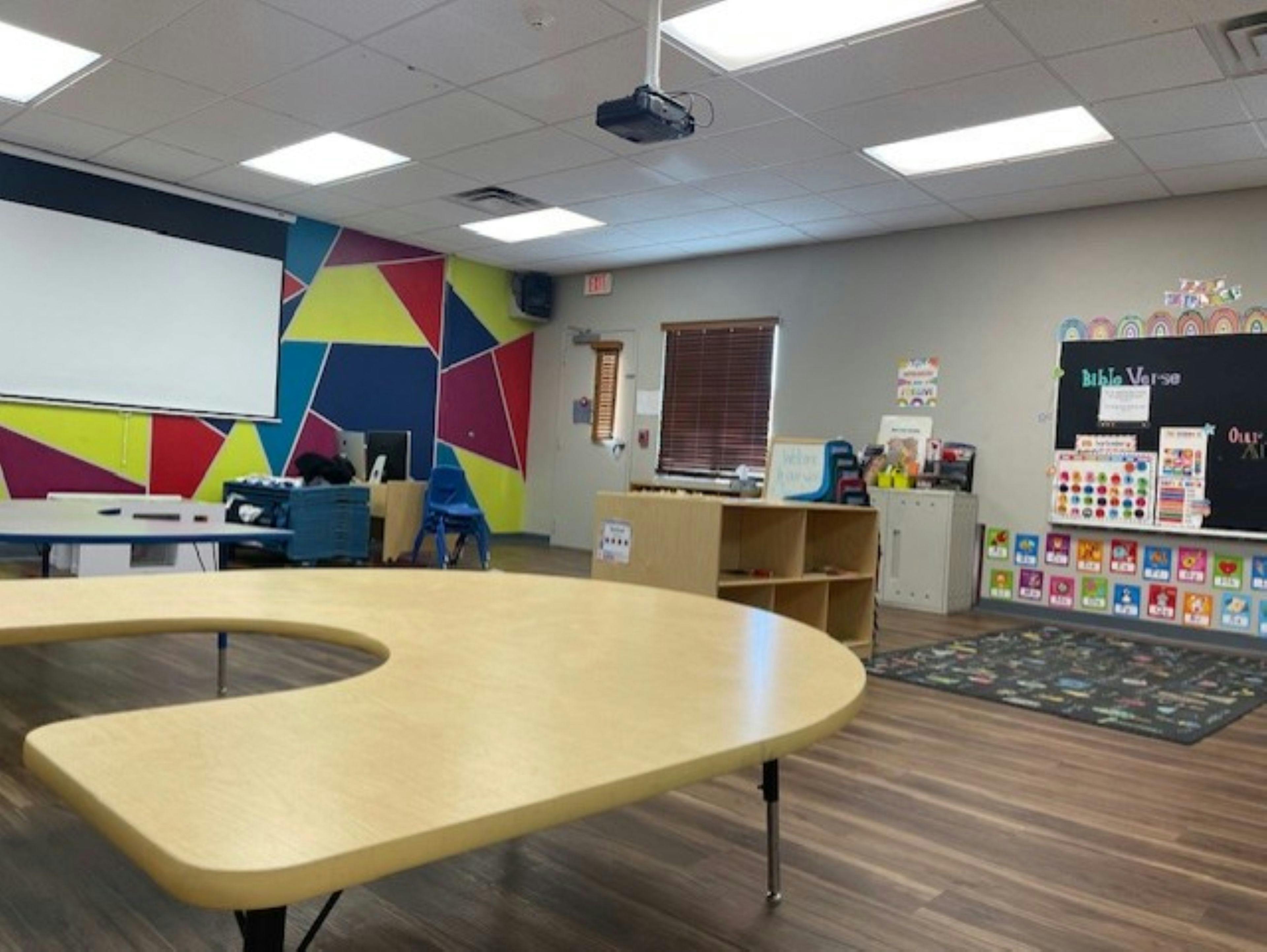 Classroom with a U-shaped table, projector screen, and colorful geometric wall