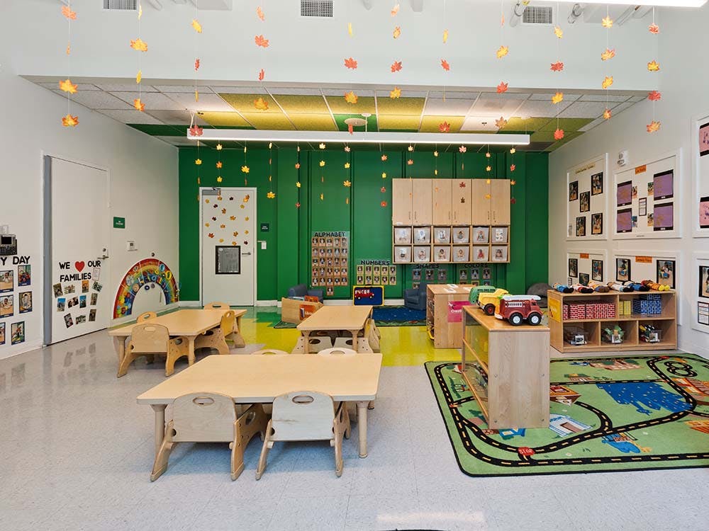 Empty classroom with small tables and chairs, toys, and autumn leaf decorations