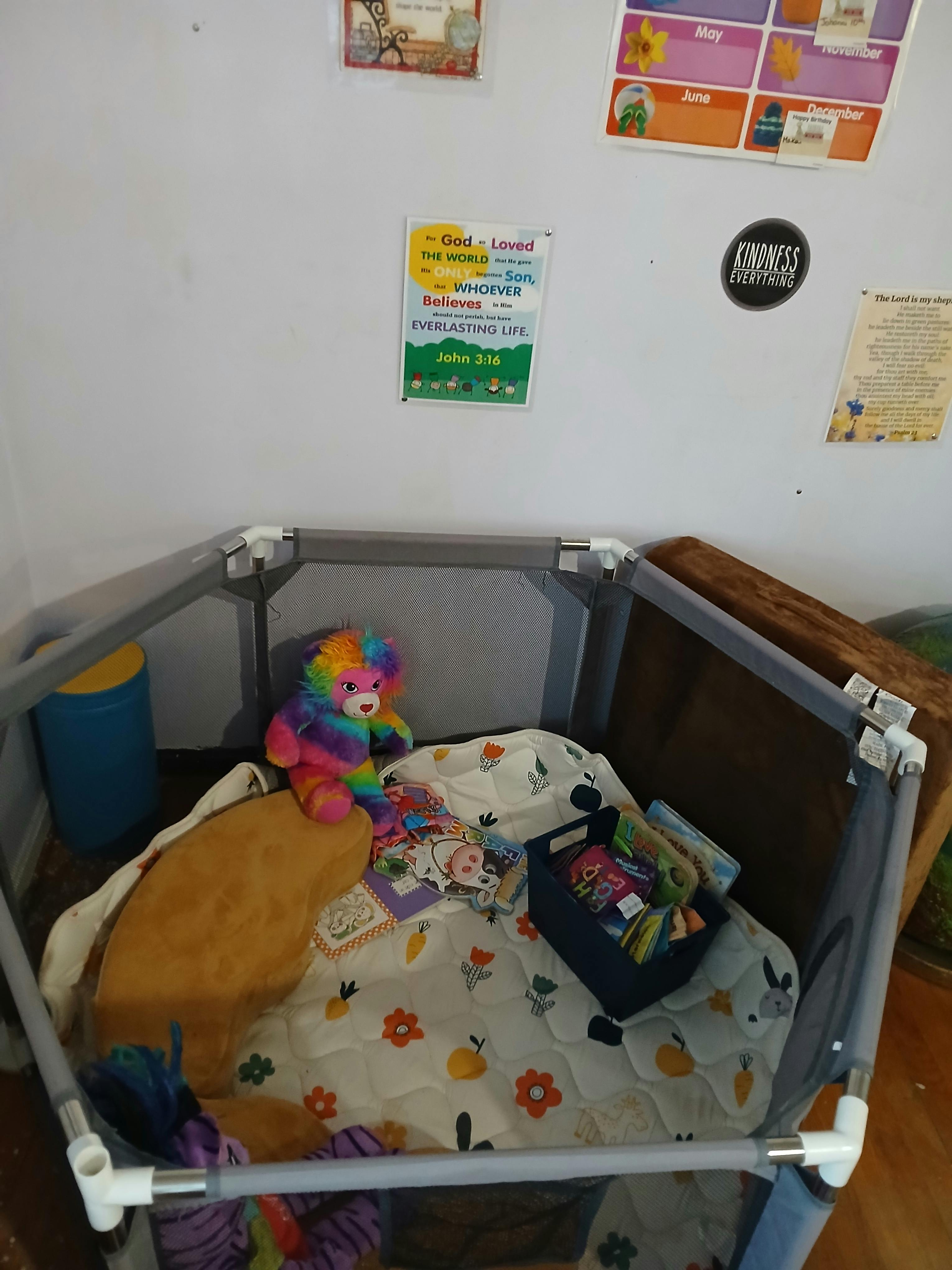 Childs playpen containing plush toys and a small storage bin filled with books