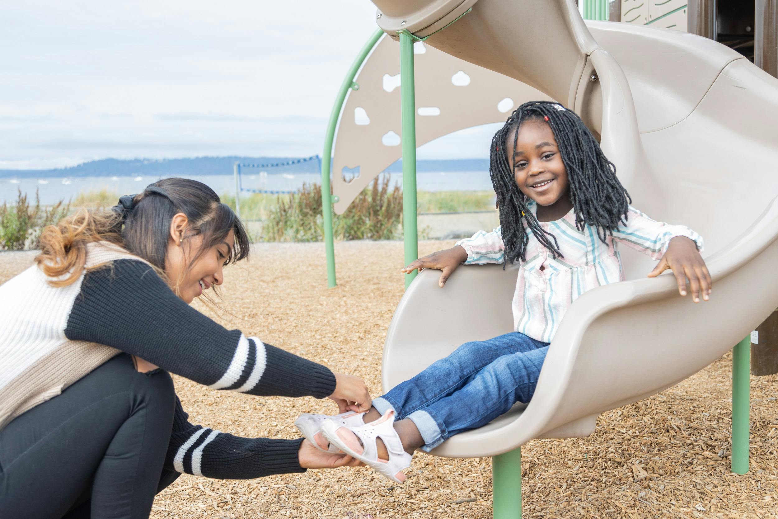 Person tying shoe of child sitting on playground slide