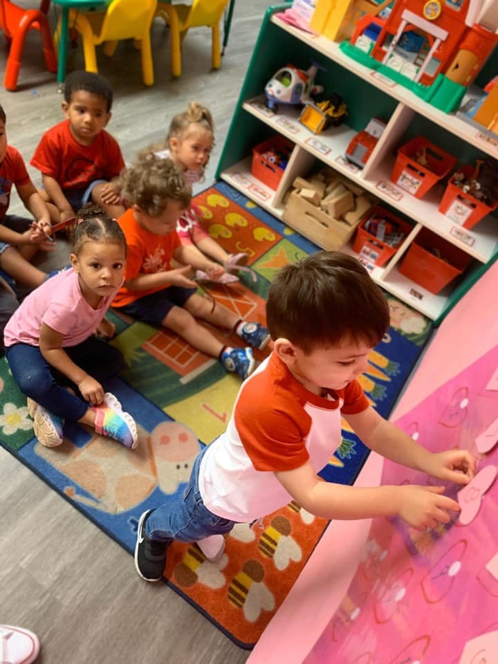 Children sitting on a rug and one child playing with a pink board
