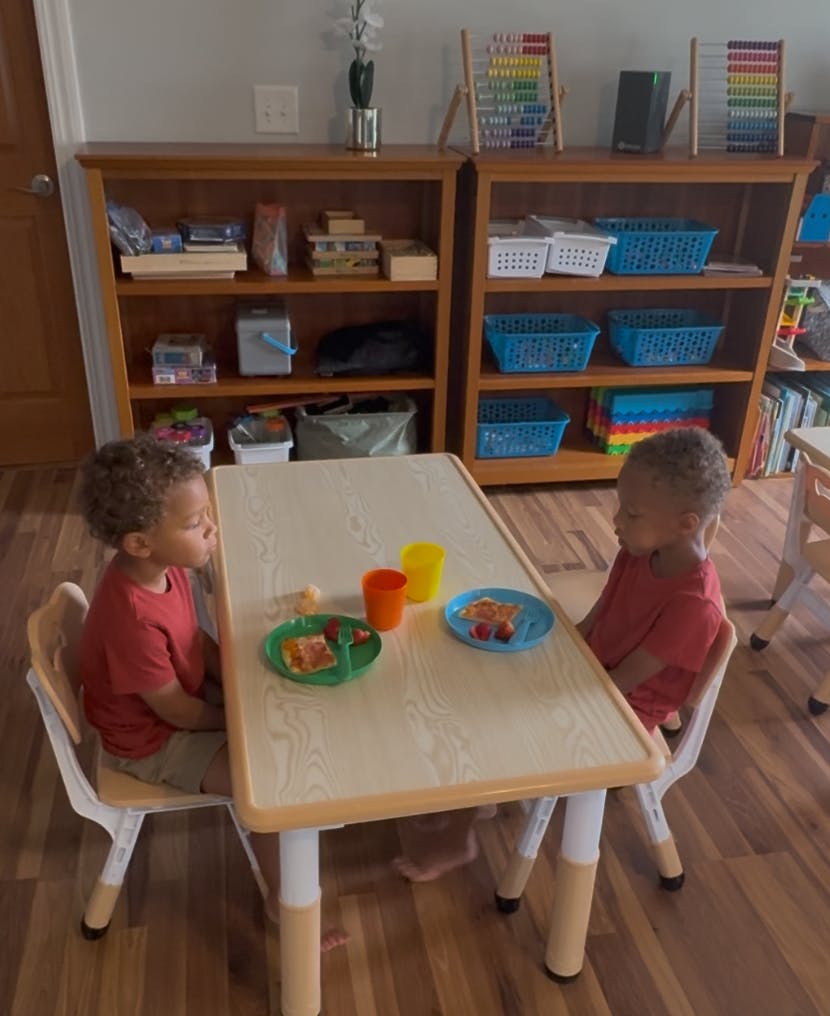 Two children sitting at a table eating snacks in a classroom setting