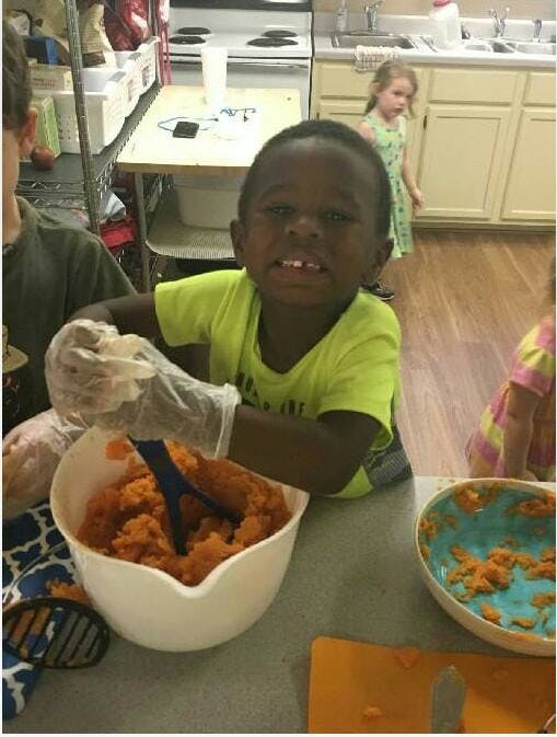 Child wearing gloves, mashing food in a bowl