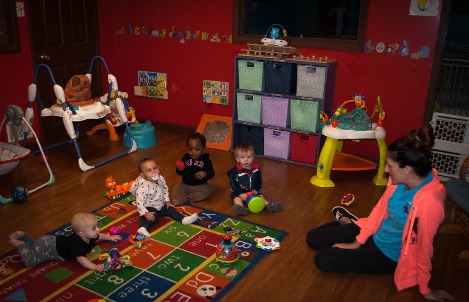Adult and multiple children playing on a rug in a room