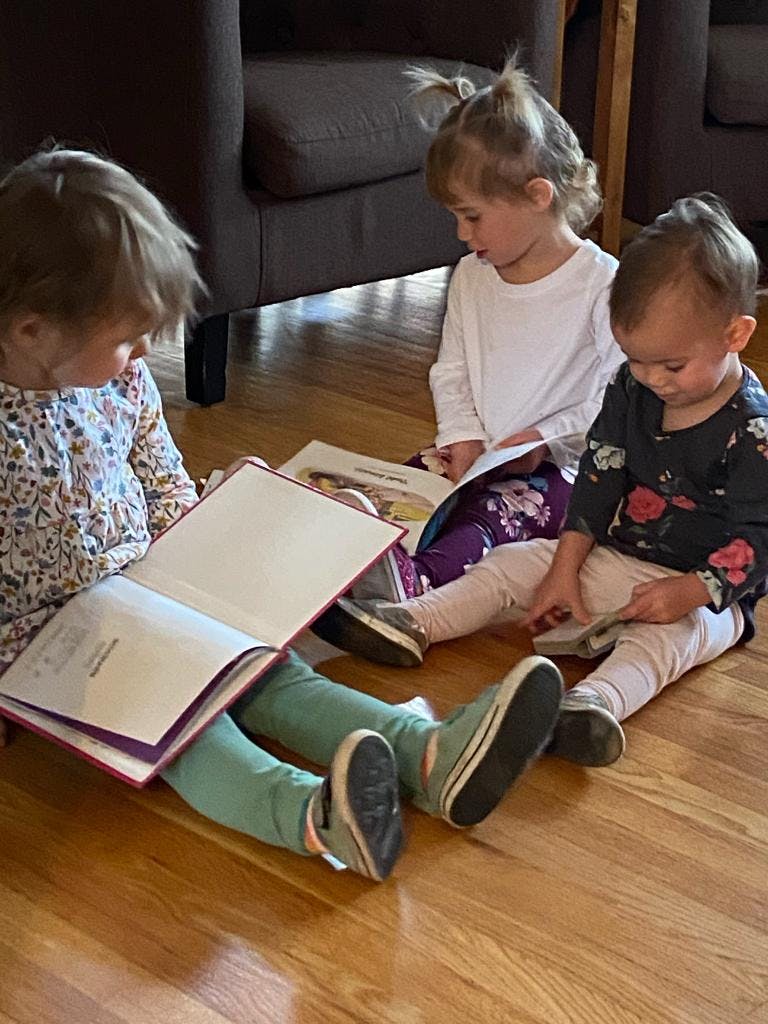 Three children sitting on a wooden floor reading books
