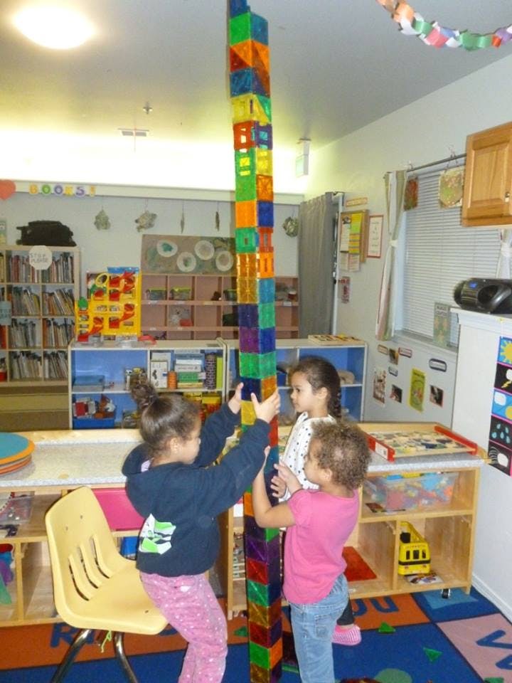 Three children building a tall tower with colorful blocks in a classroom