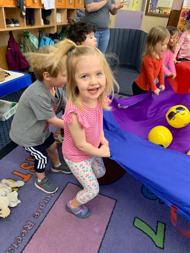 Children playing with a large purple parachute and yellow balls