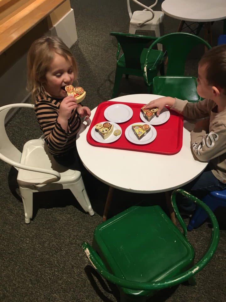 Two children at a table with toy food, heart-shaped pizza slices