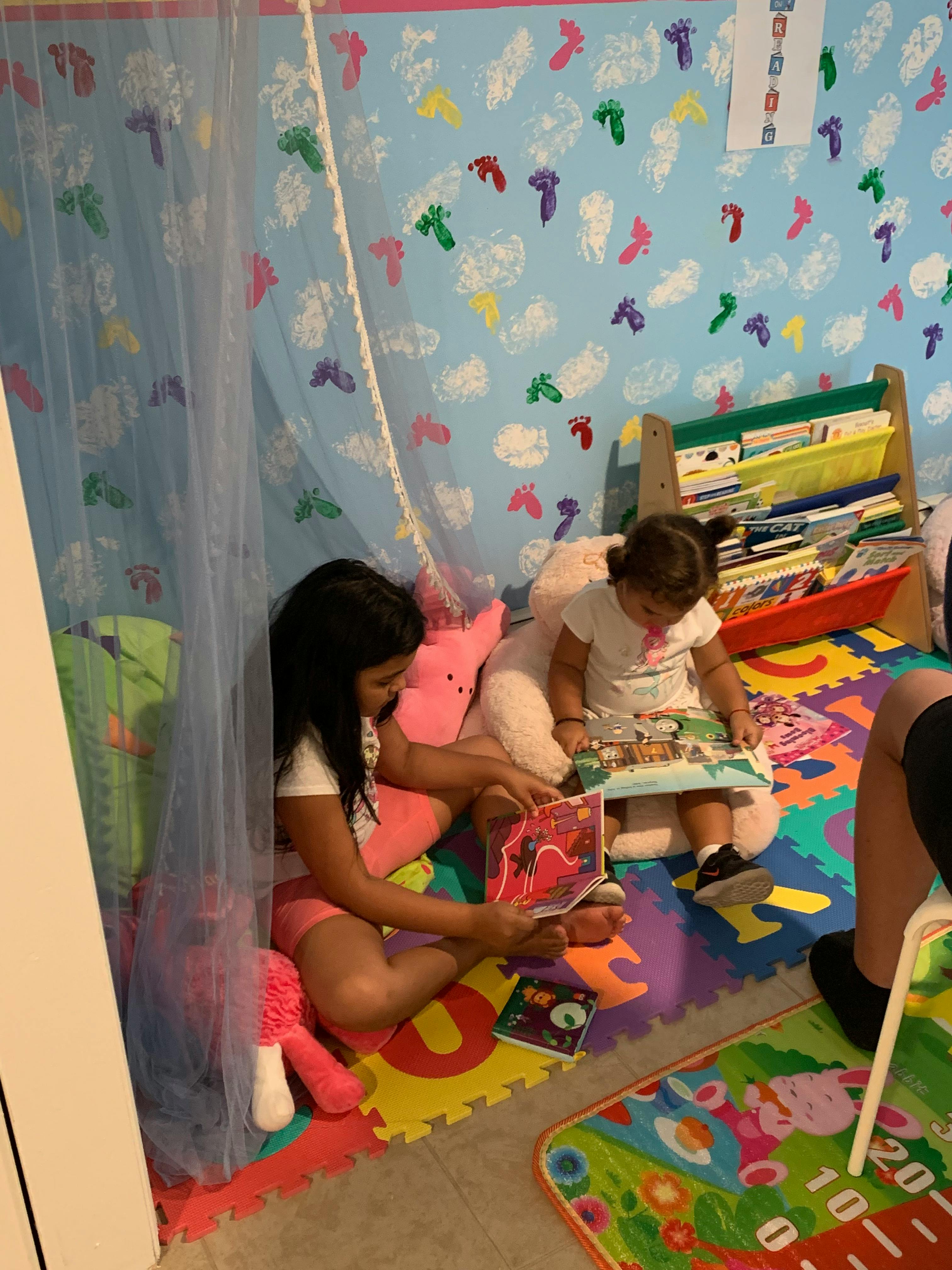 Two children sitting on a colorful mat reading books