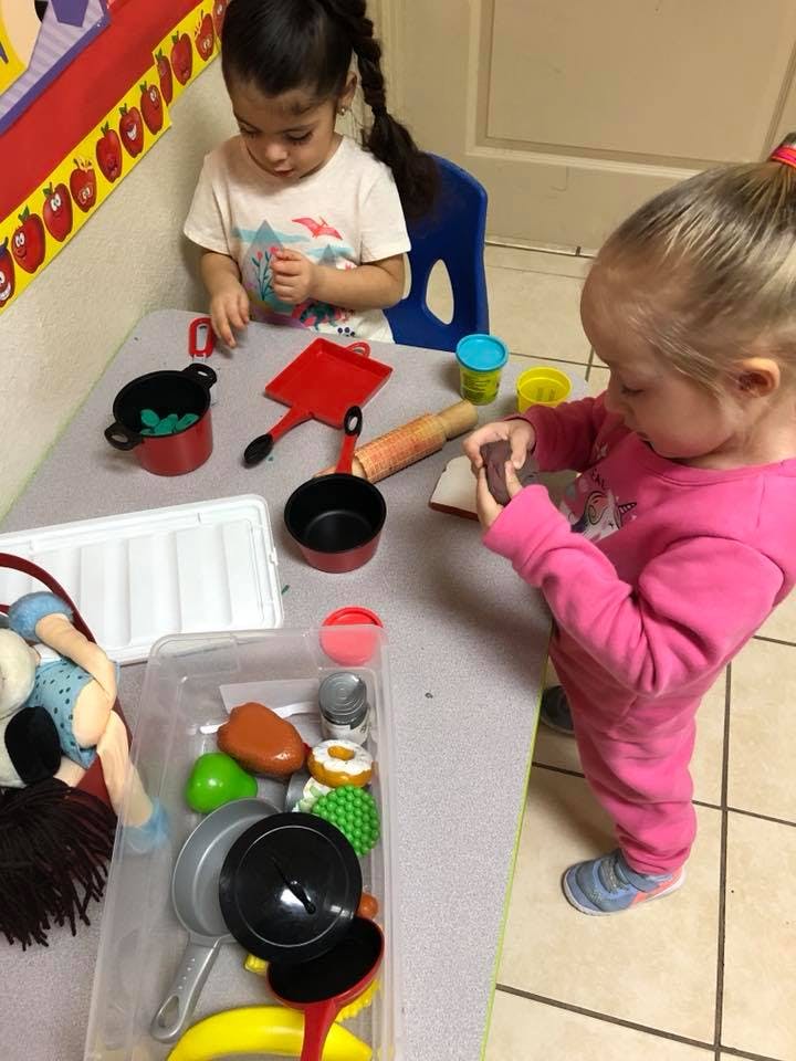 Two children playing with toy kitchen items and playdough at a table