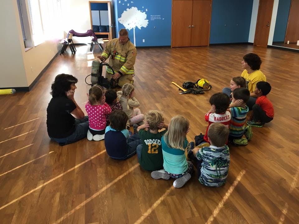 Firefighter kneeling and showing equipment to a group of children and adults