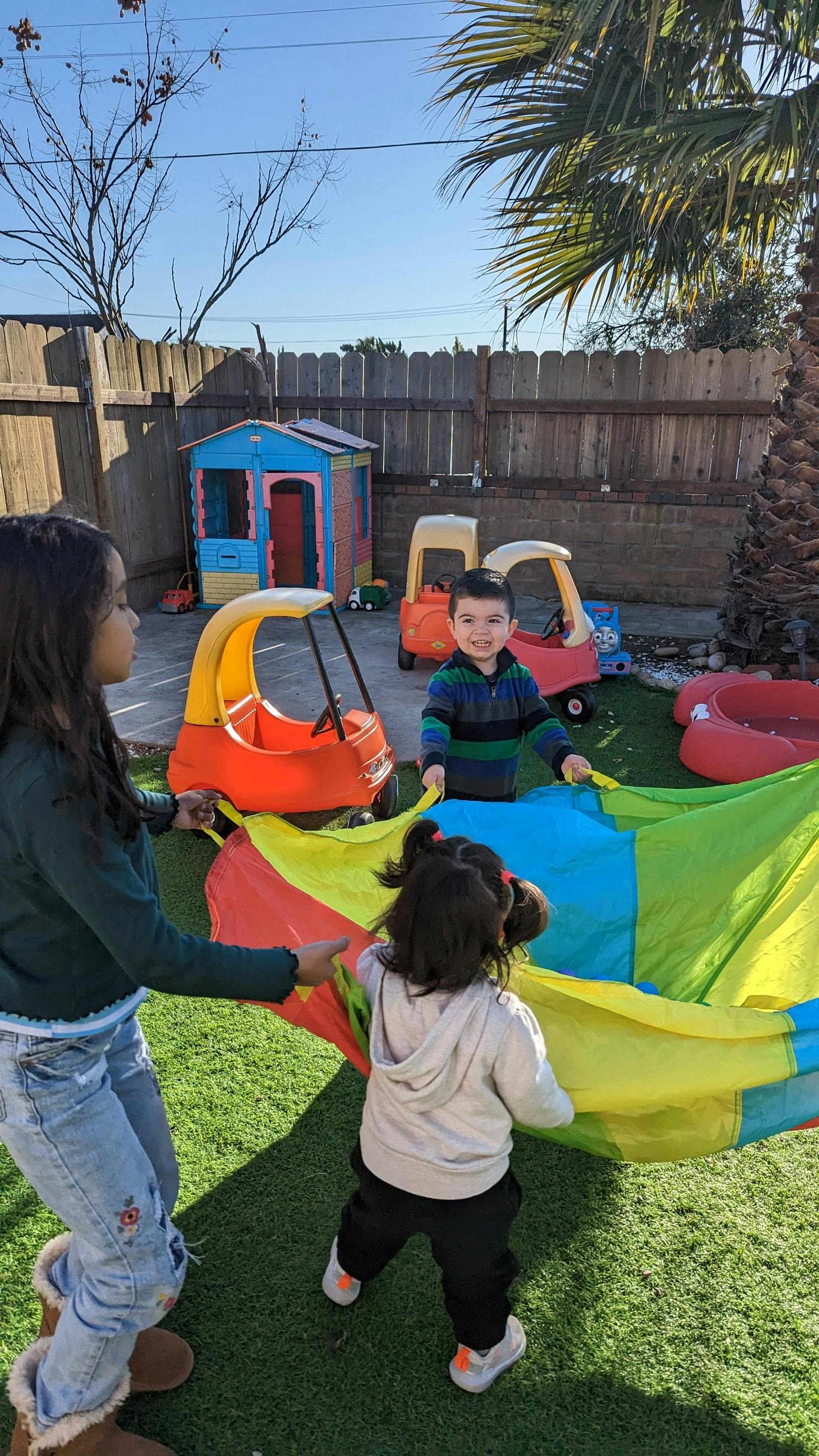 Three children playing with a colorful parachute on artificial grass