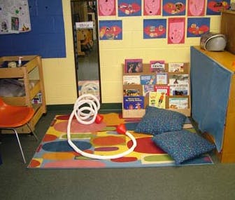Classroom reading nook with colorful rug, pillows, and book display