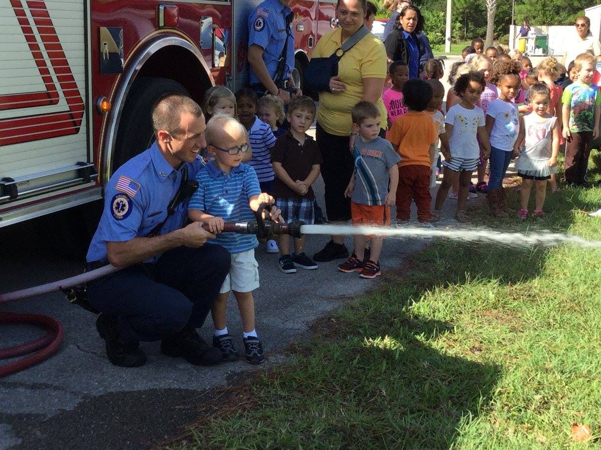 Person in uniform helping a child spray water from a hose