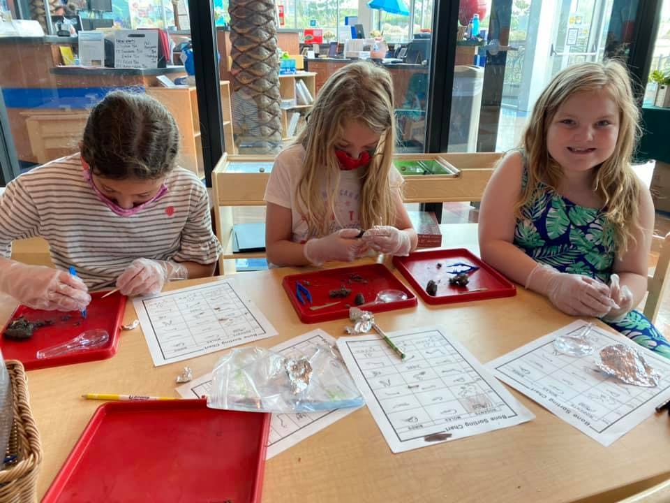 Three children wearing gloves and working on crafts at a table