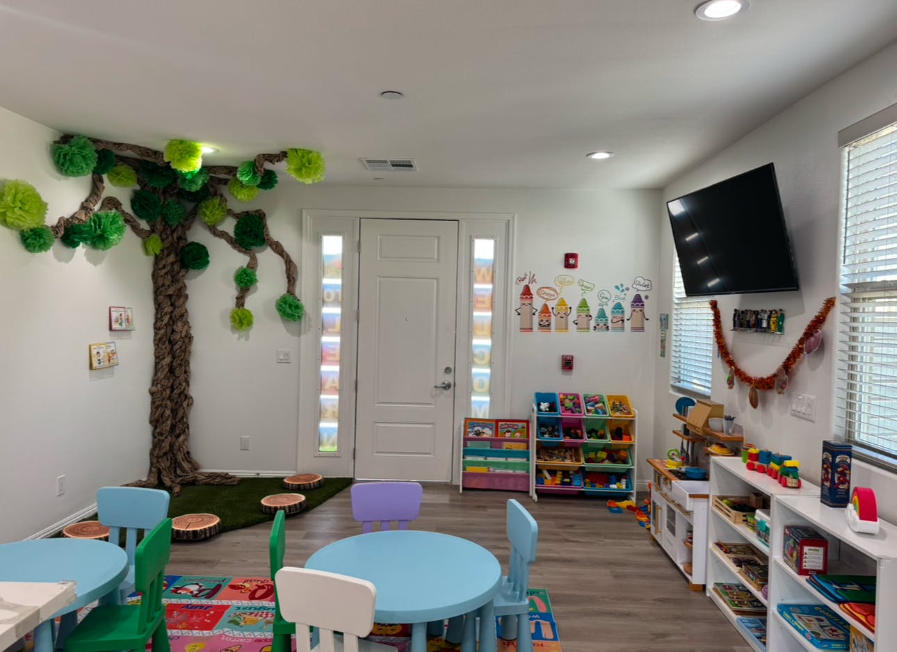 Playroom with a tree decoration on the wall, small tables, and shelves with toys
