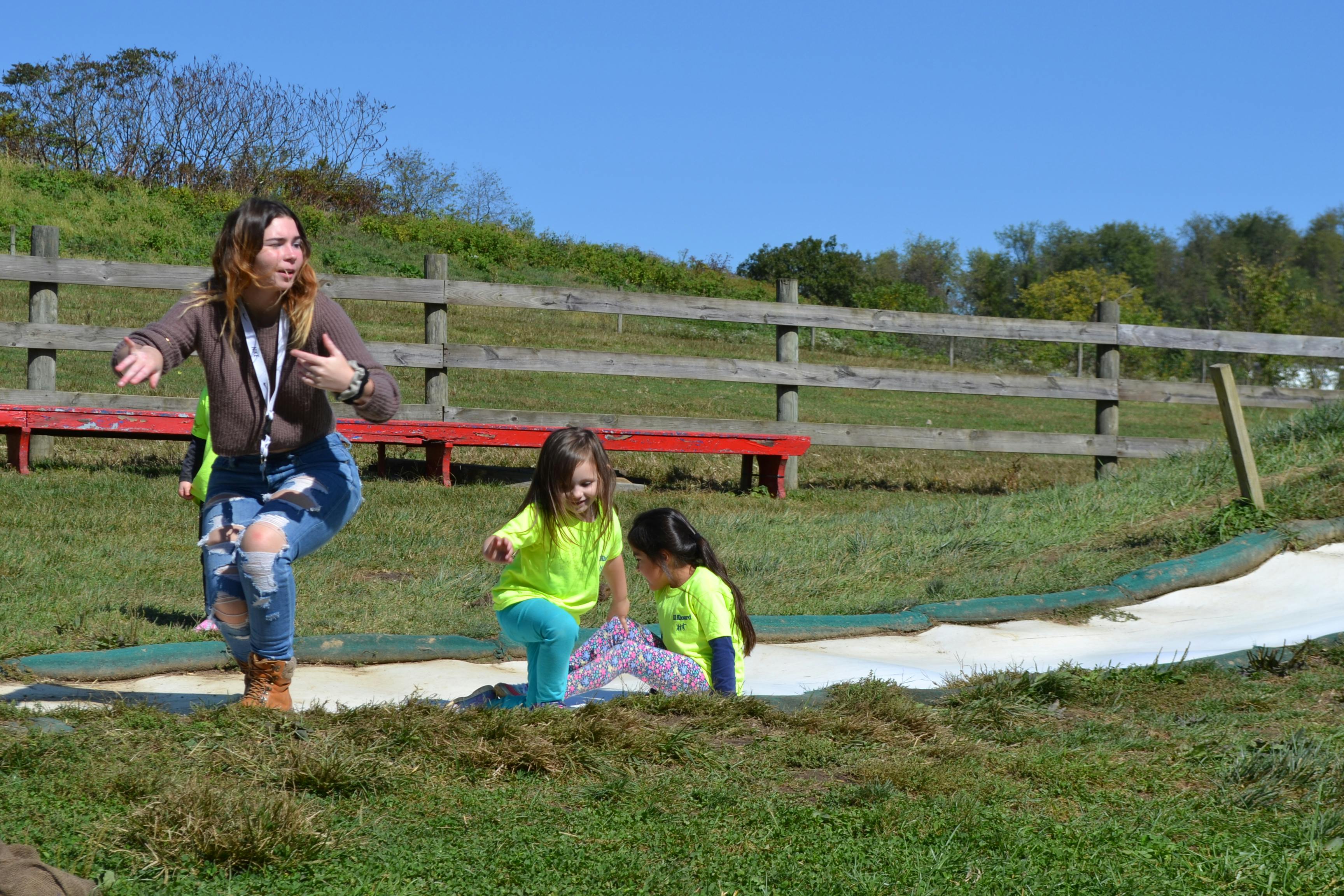 Person and two children playing on a slide in a grassy field