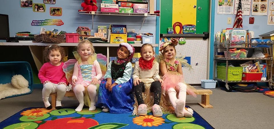 Five children in costumes sitting on a bench in a classroom