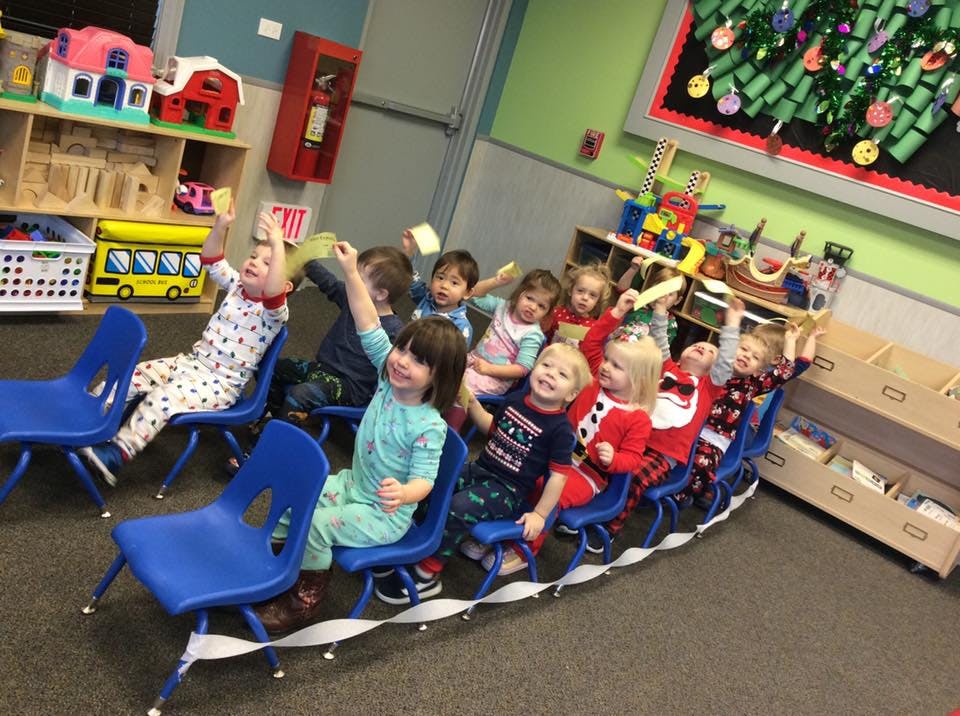 Children sitting in a line of chairs, some raising their hands