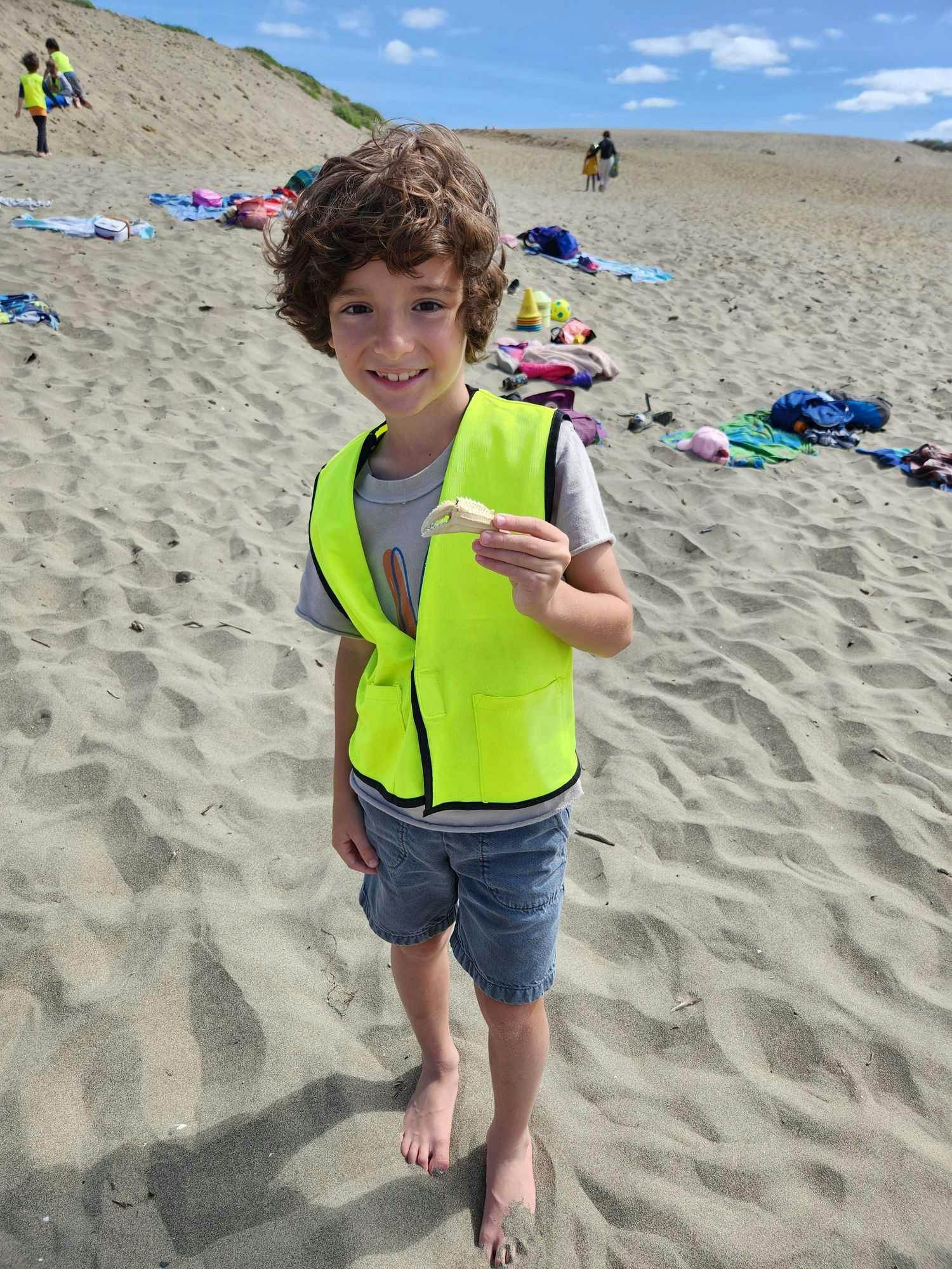 Child in a yellow vest holding a shell on a sandy beach