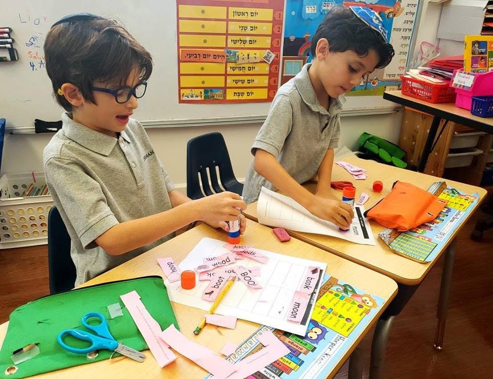 Two children working on crafts at desks in a classroom