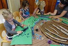 Children and adult painting sticks and paper at a table