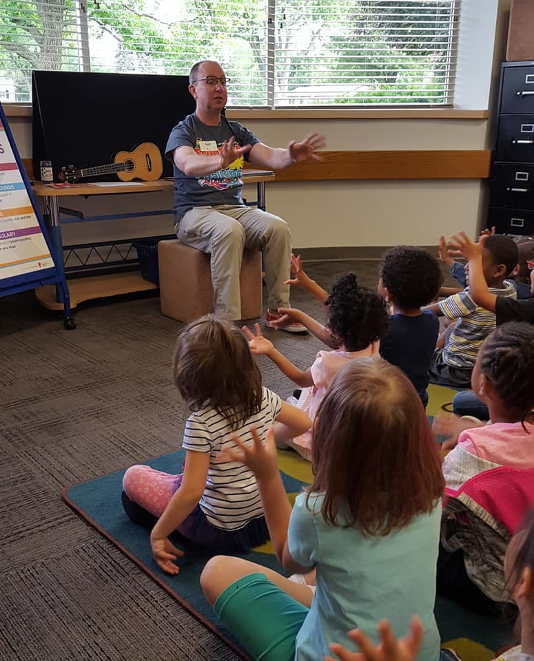 Person sitting and gesturing to a group of children