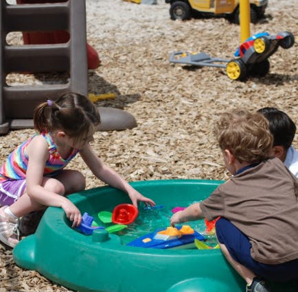 Children playing with toy boats in a water table