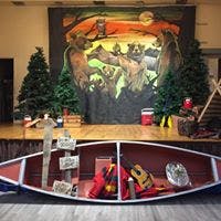 Canoe with camping gear in front of a stage with trees and a mural