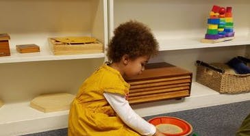 Child playing with sand in a red tray