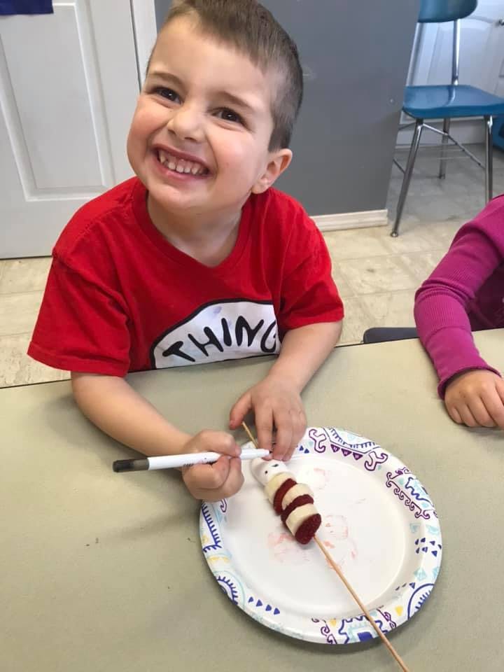 Child in red shirt decorating a banana and strawberry skewer
