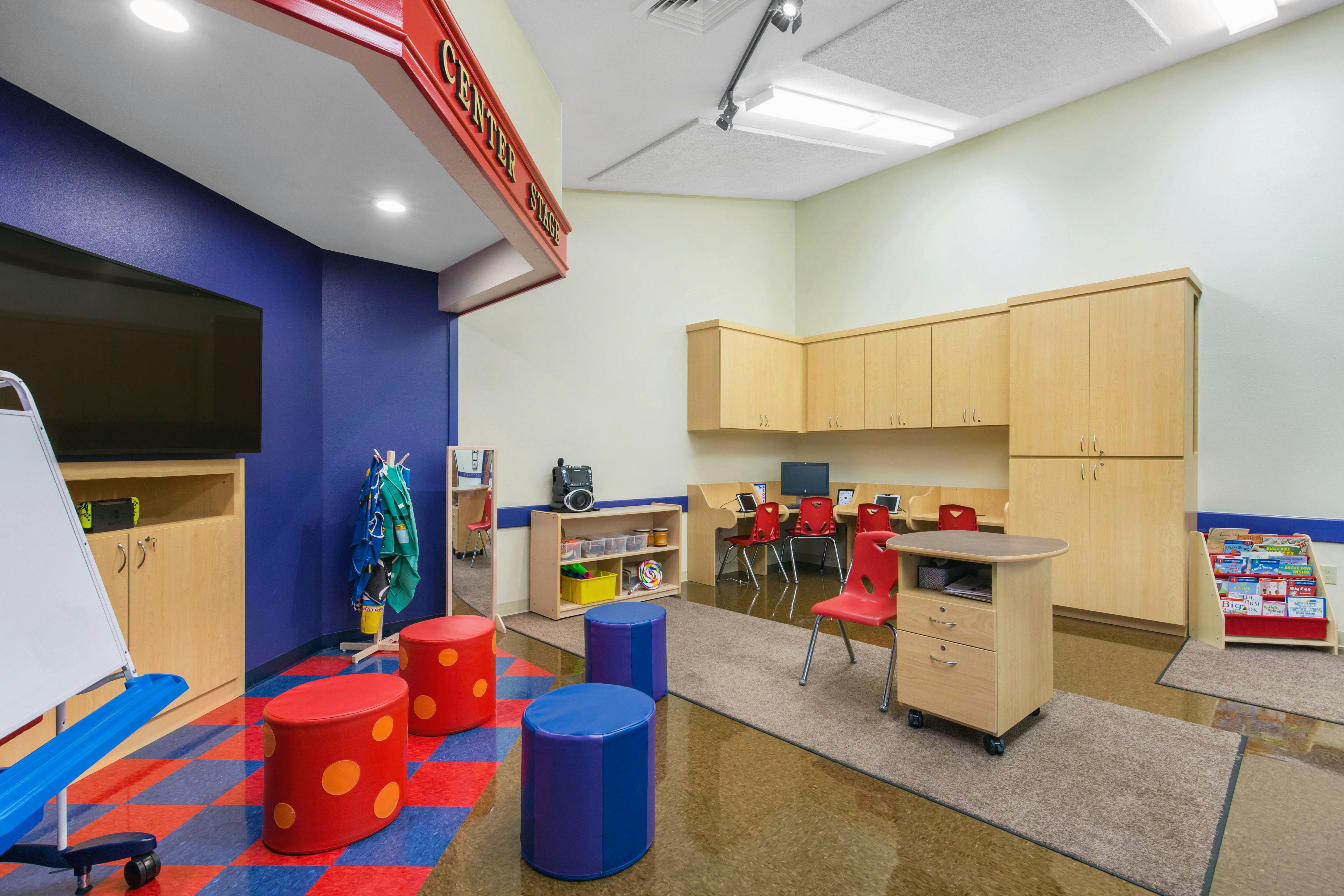 Children's classroom with small red chairs, computers, and colorful stools