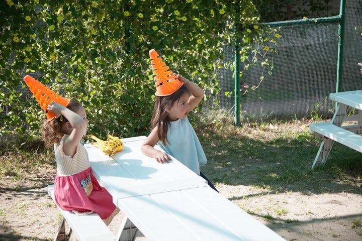 Two children sitting at a picnic table with orange cones on their heads