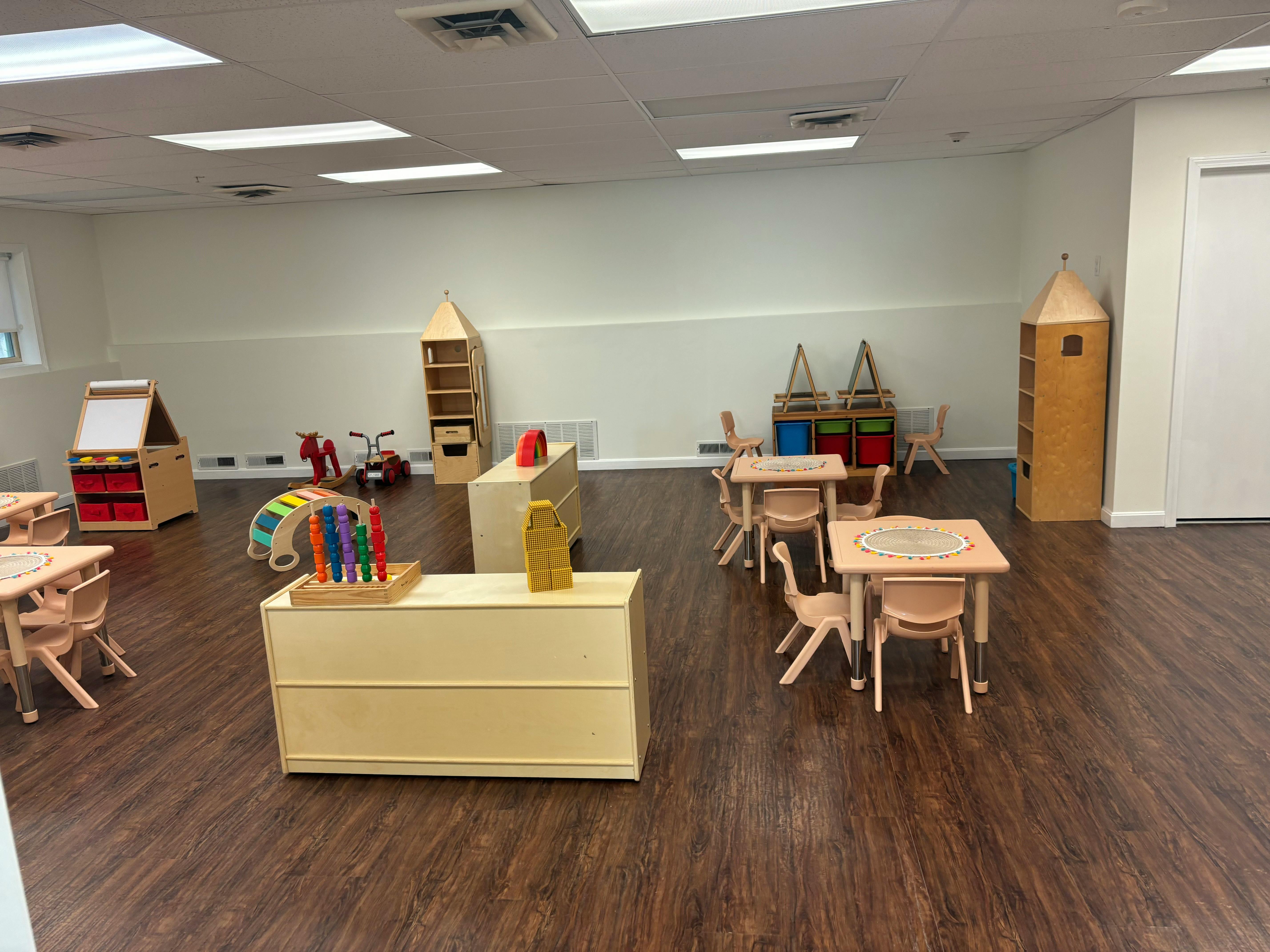 Empty classroom with small wooden tables and chairs, shelves, and play equipment