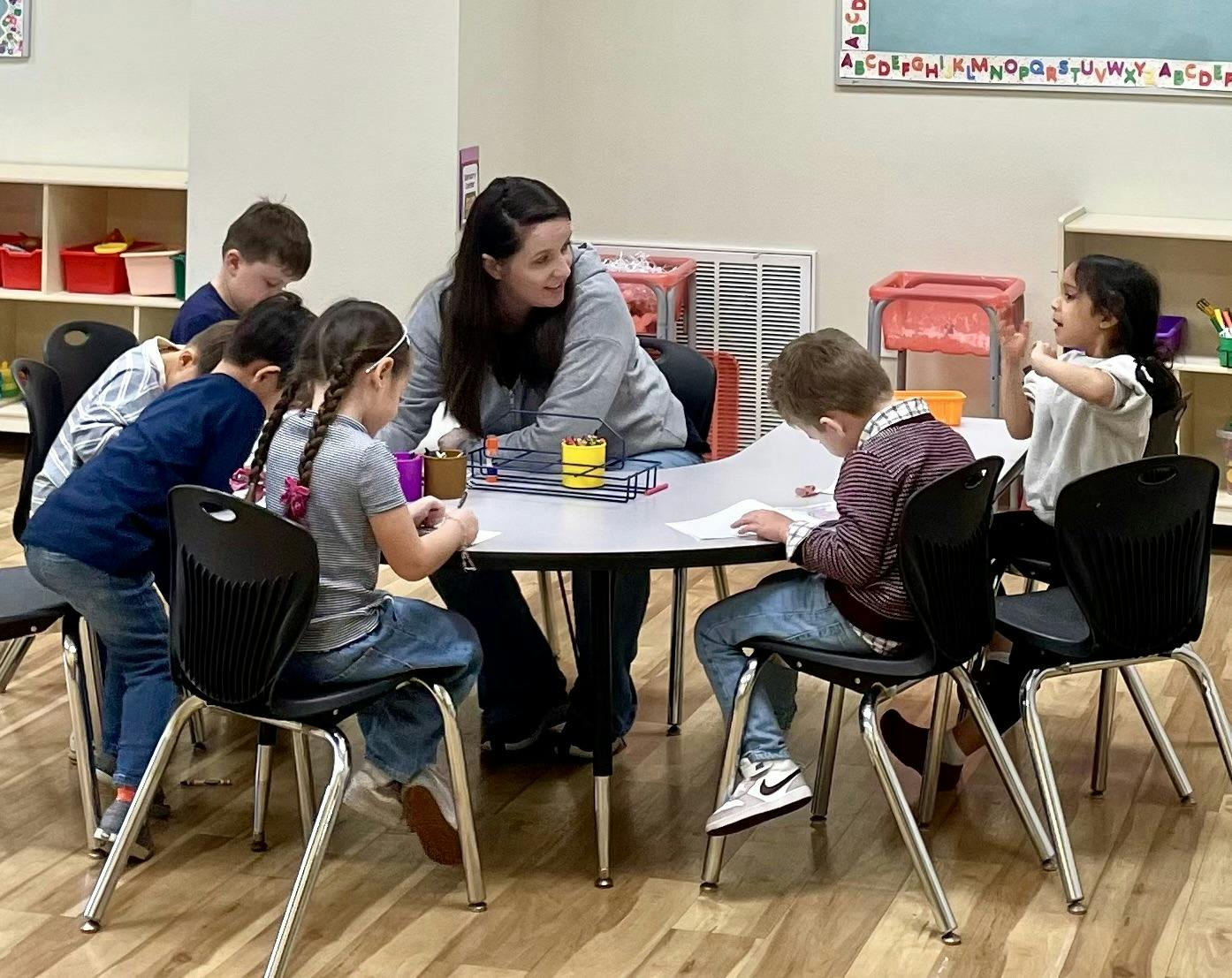 Adult and multiple children seated at a table in a classroom