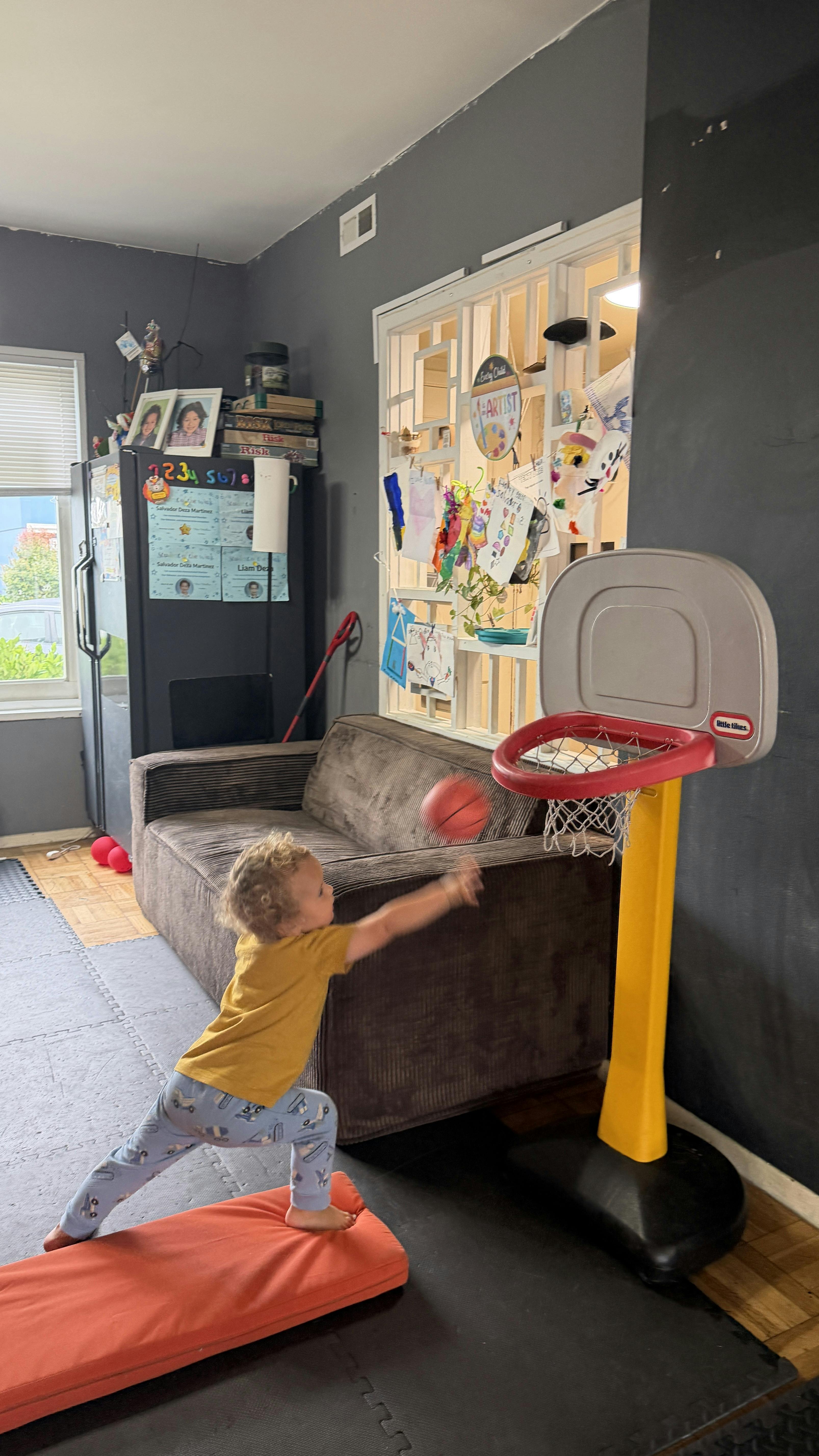 Child throwing a small basketball into a toy hoop in a living room